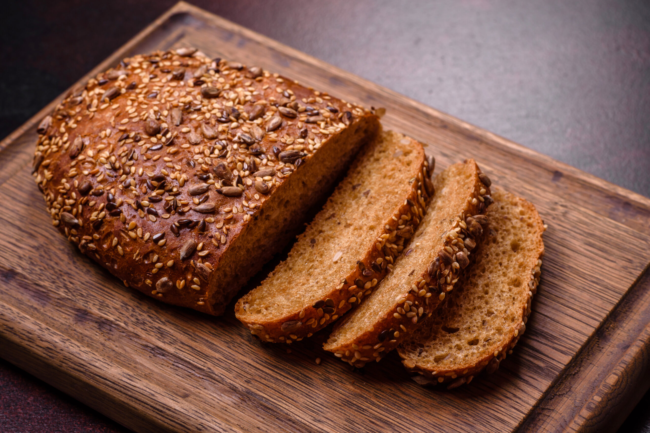 Delicious crispy bread with cereals on a wooden cutting board on a dark concrete background